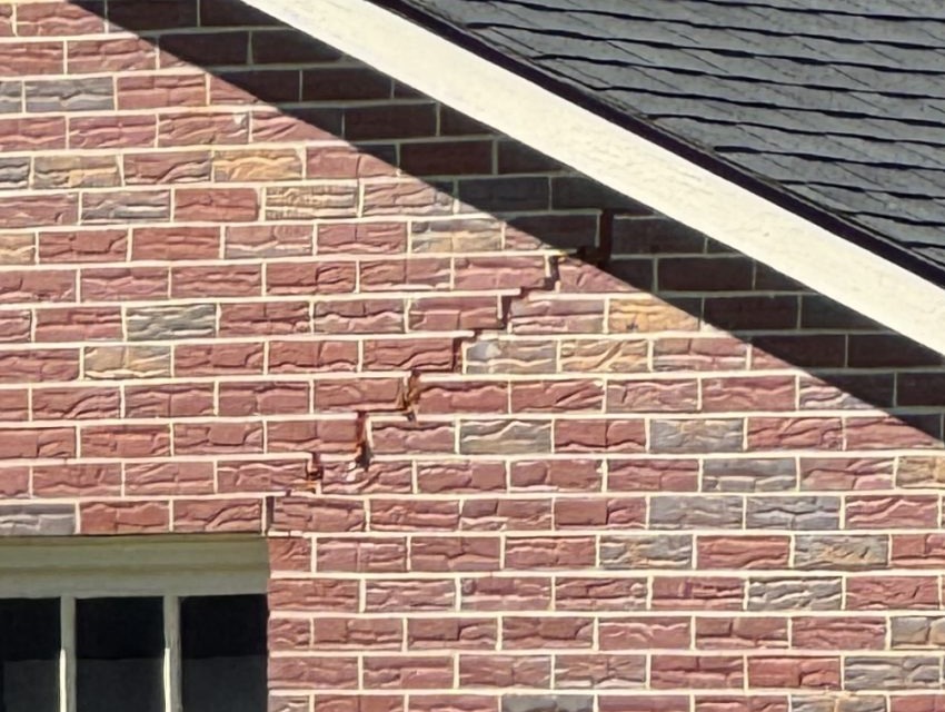 A stepped brick crack that breaks through individual bricks below a gable
