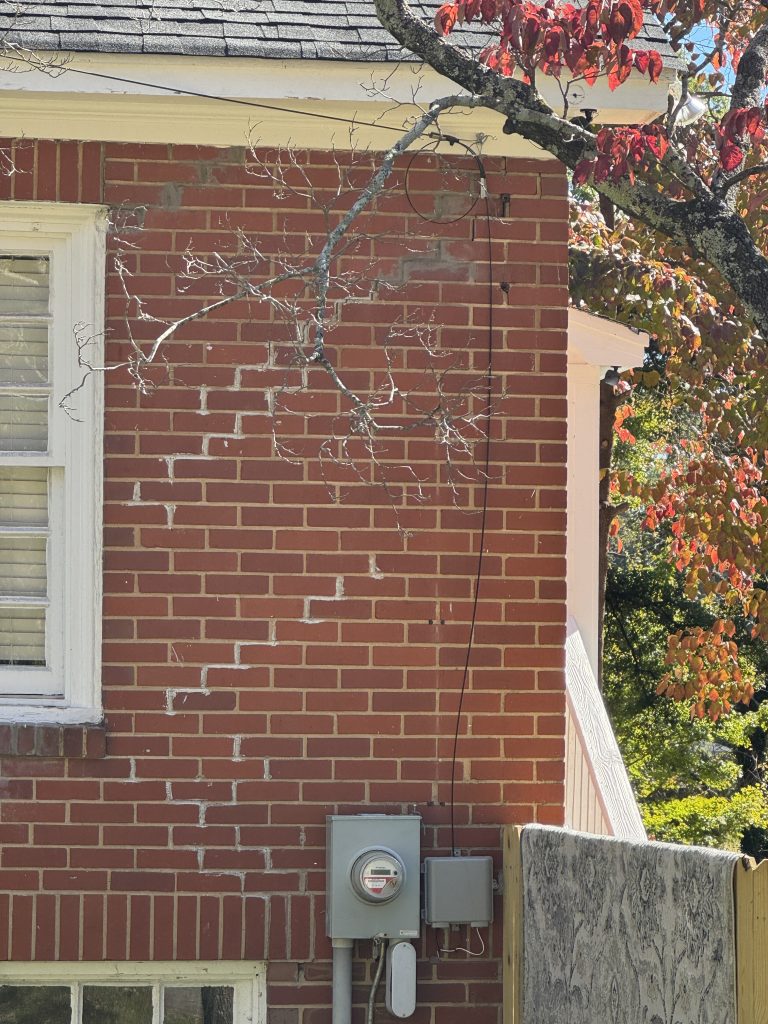 A stair-step crack stepping down the mortar joints at the corner of a brick home